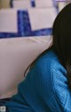 A woman in a blue sweater sitting on a bed.