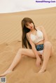 A woman sitting on top of a sand dune in a bikini.