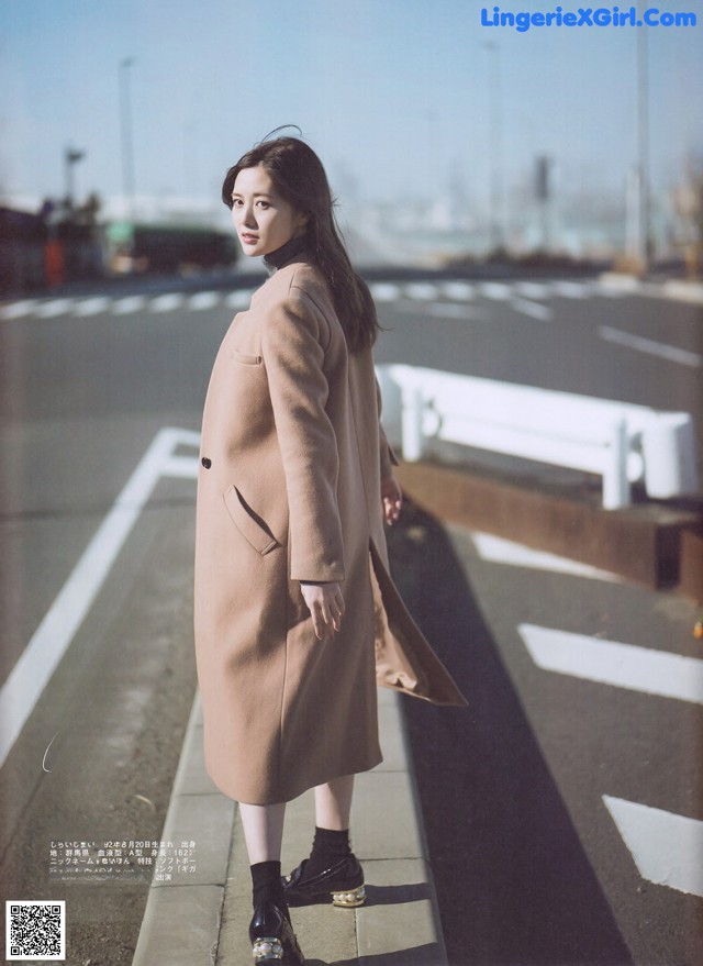 A woman in a beige coat is standing on a sidewalk.
