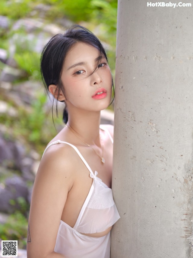 A woman in a white dress leaning against a wall.