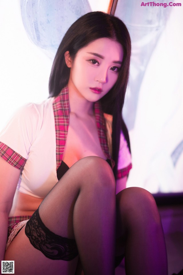 A woman in a school uniform sitting on a bed.