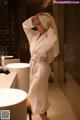 A woman in a white robe standing in a bathroom.