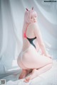 A woman with pink hair sitting on a bed.