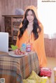 A woman in an orange hooded towel sitting at a table with a laptop.