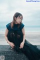 A woman in a black dress sitting on a concrete wall.