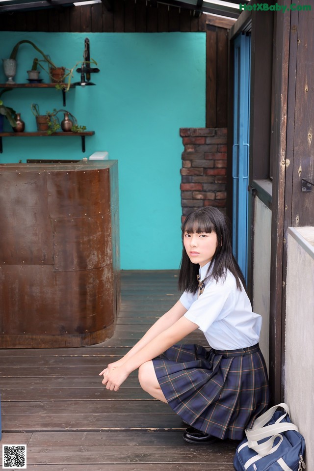 A woman in a school uniform crouching on a wooden floor.